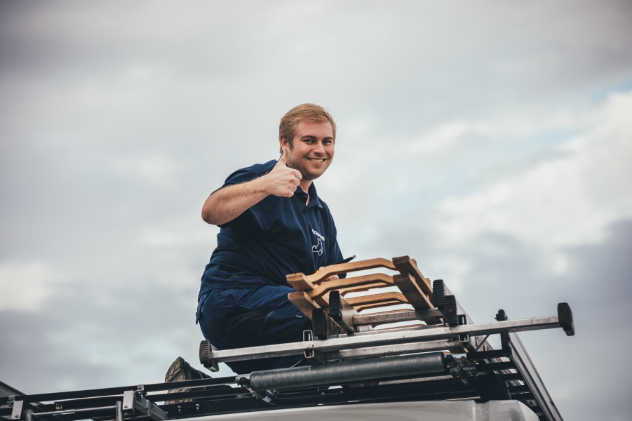 Monteur auf Fahrzeug zeigt Daumen hoch mit Holzleiter