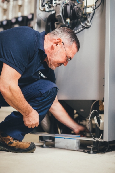 Techniker kniet vor Heizungsanlage und führt Wartung durch