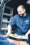 Lächelnder Mitarbeiter übergibt Kiste mit Material im Lieferwagen