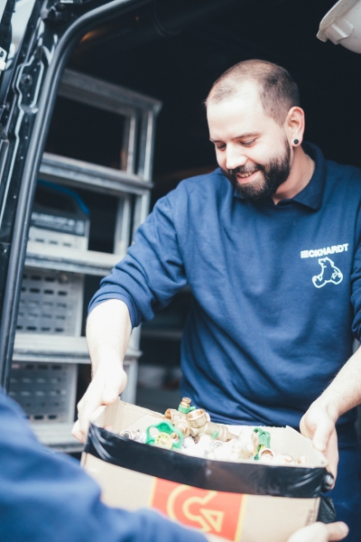 Lächelnder Mitarbeiter übergibt Kiste mit Material im Lieferwagen