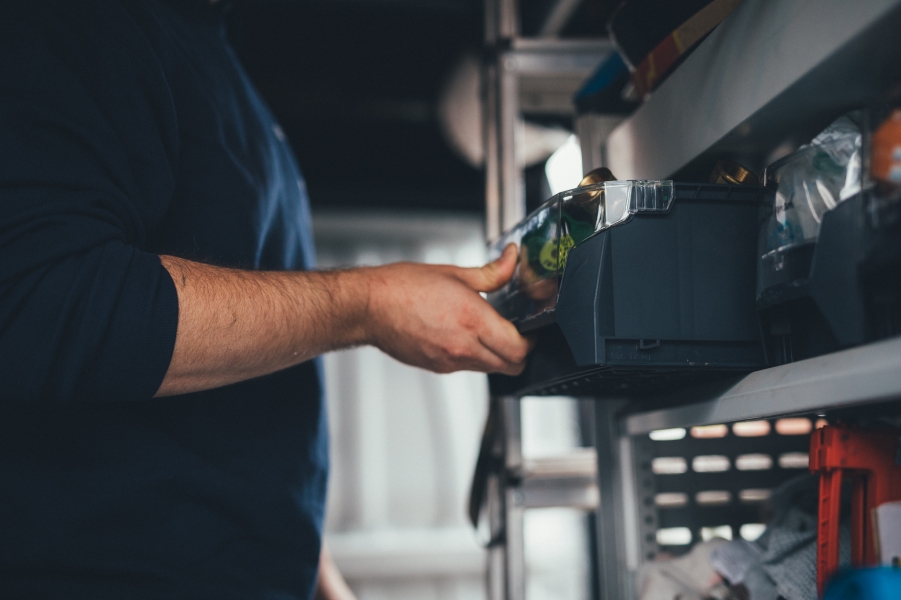 Hand greift Ersatzteil aus Regal im Lager