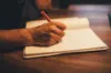 Hand schreibt mit rotem Stift in ein geöffnetes Notizbuch