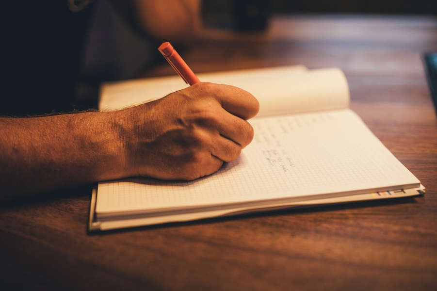 Hand schreibt mit rotem Stift in ein geöffnetes Notizbuch