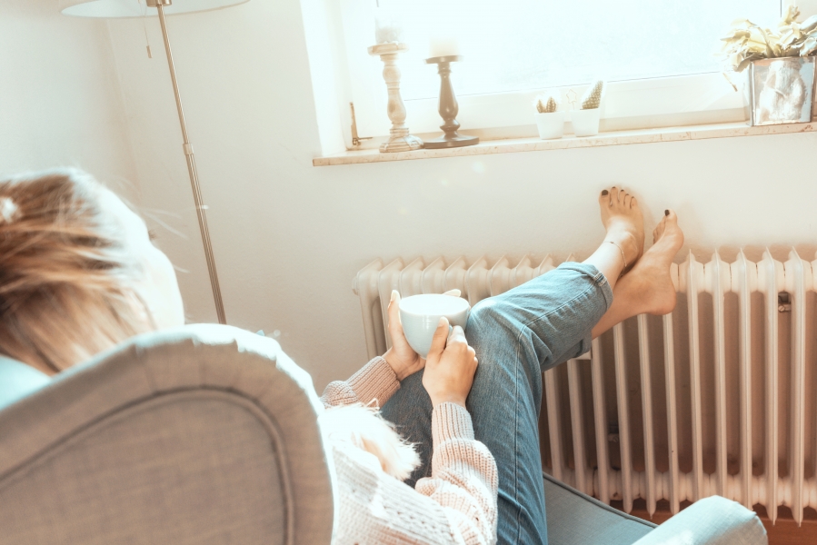 Frau entspannt mit Tasse am Heizkörper im Sonnenlicht