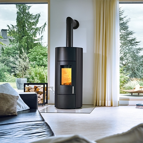 Schwarzer Kaminofen mit Flamme in hellem Wohnzimmer mit Gartenblick