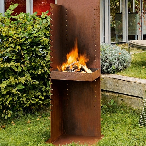 Hoher Außenkamin aus Metall mit brennendem Holz in Gartenanlage