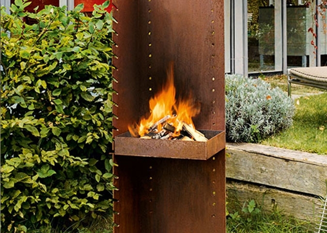 Brennende Gartensäule aus Metall mit Feuerholz im modernen Garten