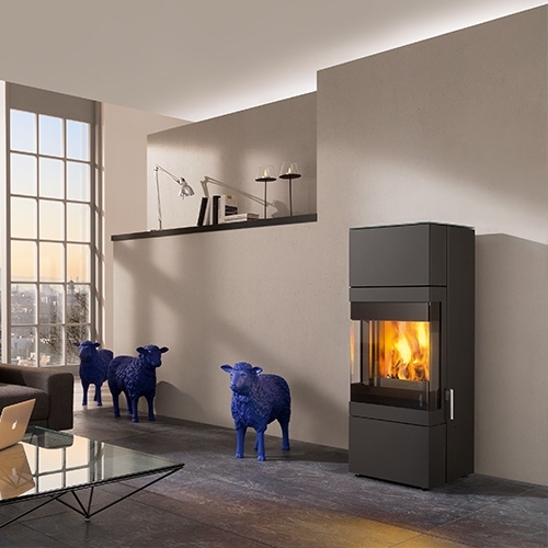 Schwarzer Kaminofen mit Flamme, davor drei blaue Schafskulpturen