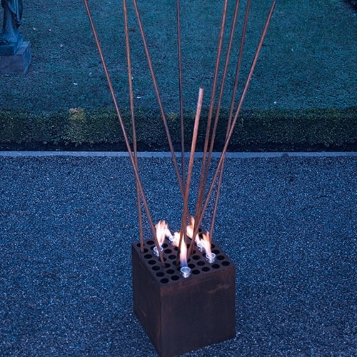 Stahlwürfel mit langen Flammenstäben im Außenbereich bei Dämmerung
