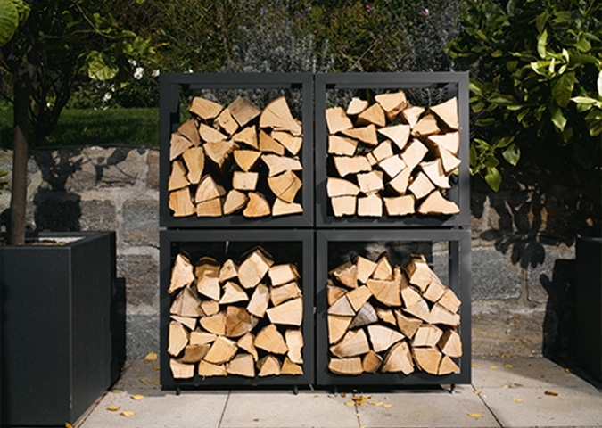 Sauber gestapeltes Kaminholz in vier schwarzen Regalfächern draußen