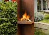 Brennende Gartensäule aus Metall mit Feuerholz im modernen Garten